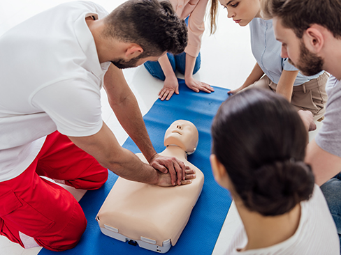 instructor performing cpr on dummy during first aid training with group of people