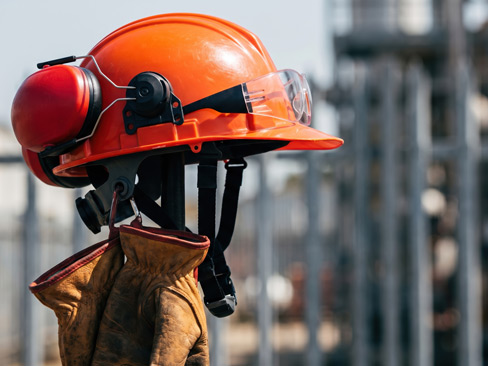 Construction safety helmet with protective goggles, ear protection and work gloves at building site. Personal protective equipment for industrial work, construction safety and workplace protection.